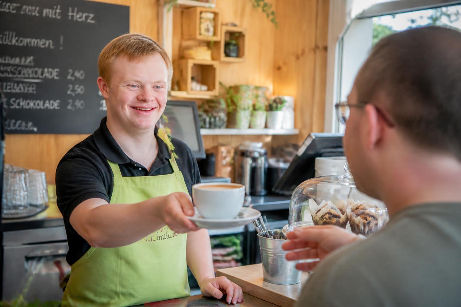 Inklusionscafé – Barista übergibt Kaffee